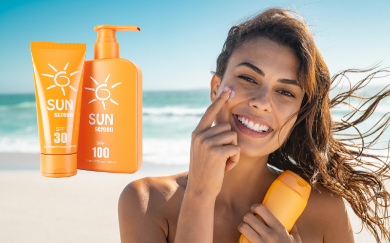 woman on beach applying sunscreen on face with sunscreen bottle