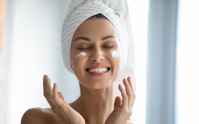 woman with hair in towel and applying cream on face