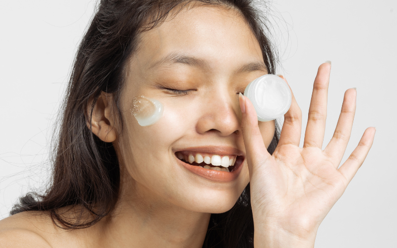 smiling woman with cream on face, and small box in hand